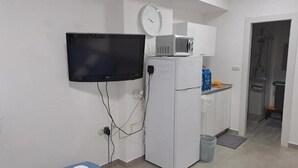 A small kitchenette with a TV, microwave, and refrigerator. There is a small trash bin and a towel on a bench. - Studio in Modi'in center (Modi'in-Maccabim-Re'ut)