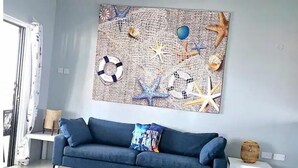 Una sala de estar con un sofá azul, un tapete estampado y una obra de arte con motivos marinos.