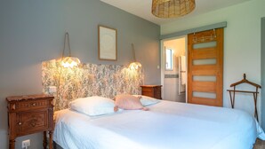 A bedroom with a bed, two bedside lamps, a nightstand, a wooden wardrobe, and a hanging rack.