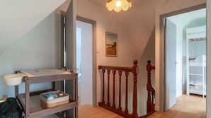 A hallway with a wooden staircase, a baby changing station, and a white shelving unit.