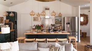 Une cuisine moderne dotée d’un îlot central, de luminaires suspendus et d’un réfrigérateur en acier inoxydable.