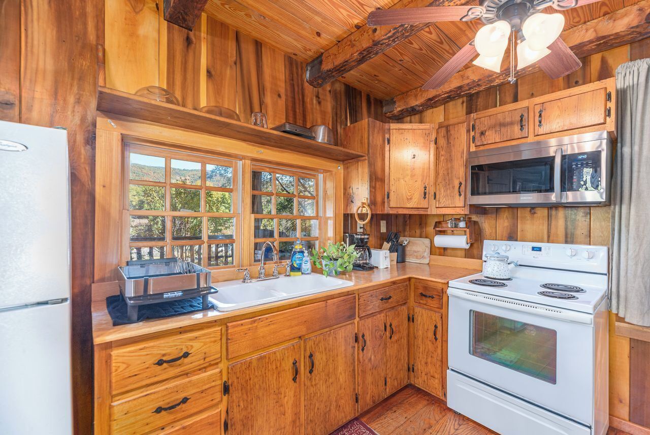A wooden cabin kitchen with a refrigerator, stove, microwave, and a large window.