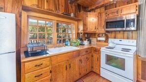A wooden cabin kitchen with a refrigerator, stove, microwave, and a large window.