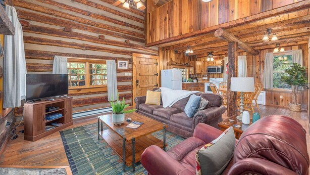 A log cabin interior with a living room, kitchen, and dining area.