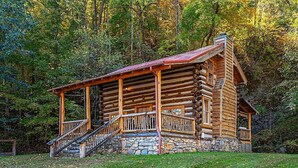 A log cabin with a stone foundation, wooden porch, and a staircase leading to the entrance.