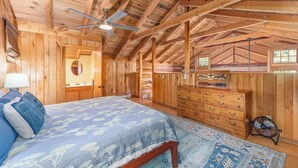 A spacious bedroom with a large bed, wooden ceiling beams, a ceiling fan, and a dresser.