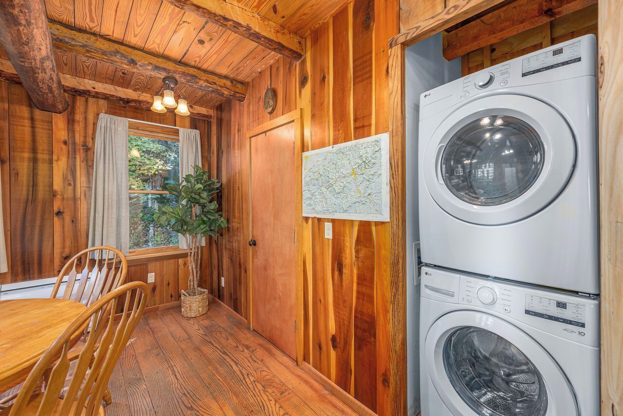 A wooden interior with a dining table and chairs, a map on the wall, and a stacked washer and dryer.