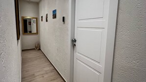 Un pasillo con una puerta blanca, un espejo y algunas fotos pequeñas en la pared.