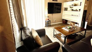 A living room with a sofa, coffee table, TV, and shelves with various items.