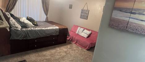 Une chambre à coucher avec un lit, un canapé et une petite table. On y trouve un ventilateur de plafond, une fenêtre avec des rideaux et un climatiseur fixé au mur.
