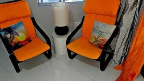 Zwei orangefarbene Sessel mit Kissen, eine weiße Lampe und ein Fenster mit Vorhängen.