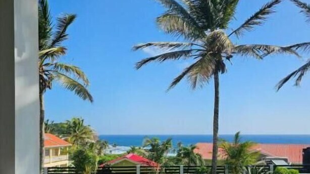 Ein Balkon mit Korbmöbeln und Blick auf das Meer und Palmen.