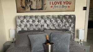 A neatly made bed with a heart-shaped arrangement of rose petals and a bottle of champagne in a bucket. - Stunning 1-bed Cottage in Halifax (Halifax)