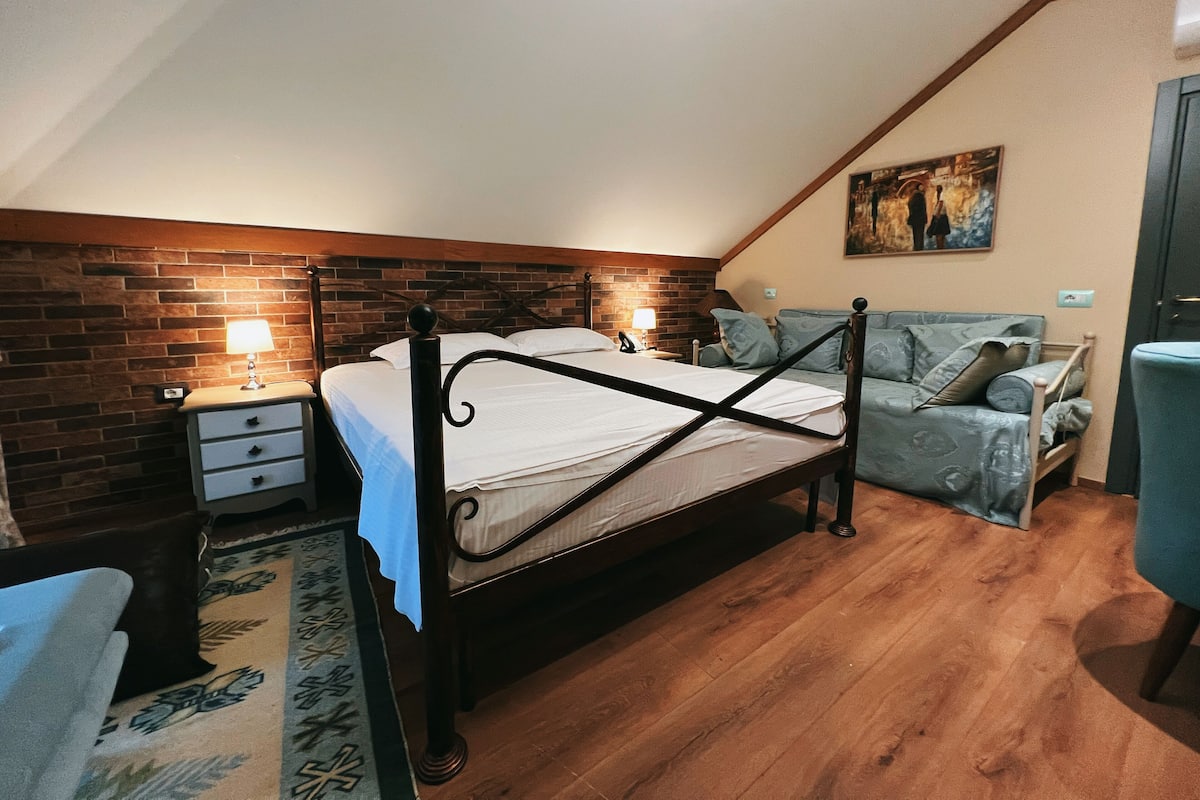 Un dormitorio con estructura de cama de madera, una mesita de noche, una lámpara, una silla azul y un cuadro en la pared.