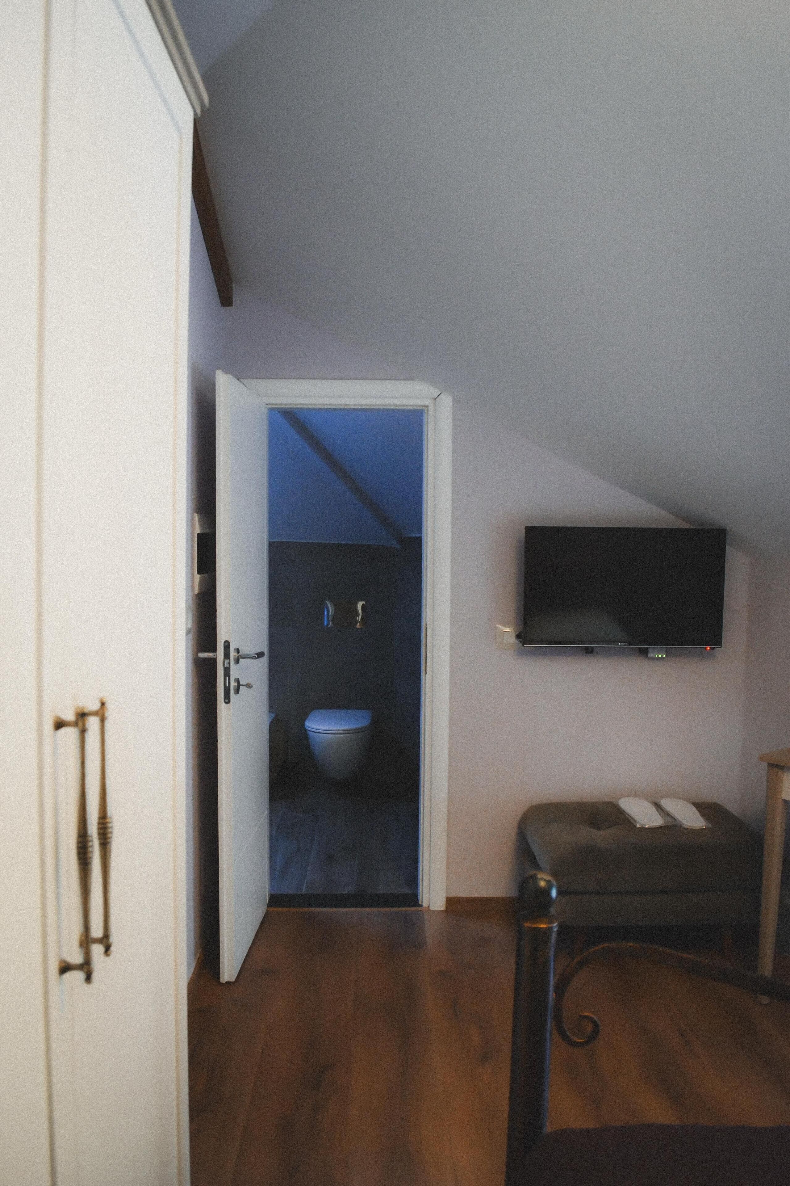 Une pièce avec un plancher en bois, une porte blanche, un téléviseur fixé au mur et un petit canapé gris.