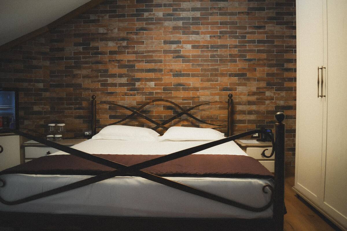 Un dormitorio con pared de ladrillo, una cama con cabecera de madera, una mesita de noche y un armario.