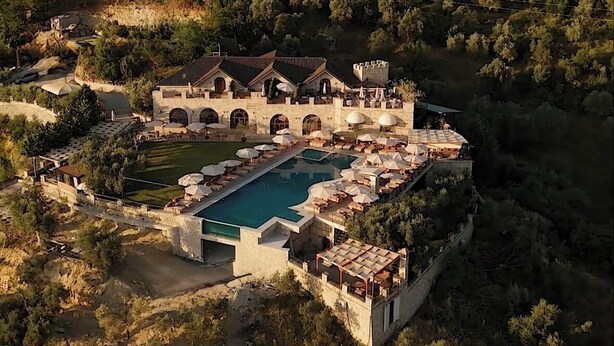 An aerial view of a resort with a central swimming pool, surrounded by lush greenery and a mountainous backdrop. - Chateau Fasel (Dajt)
