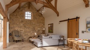 Ein rustikaler Innenraum mit freiliegenden Steinwänden, einer Lofts-Decke, einer gemütlichen Sitzecke mit Sofa und Sesseln sowie einem Esstisch, der für eine Mahlzeit gedeckt ist.