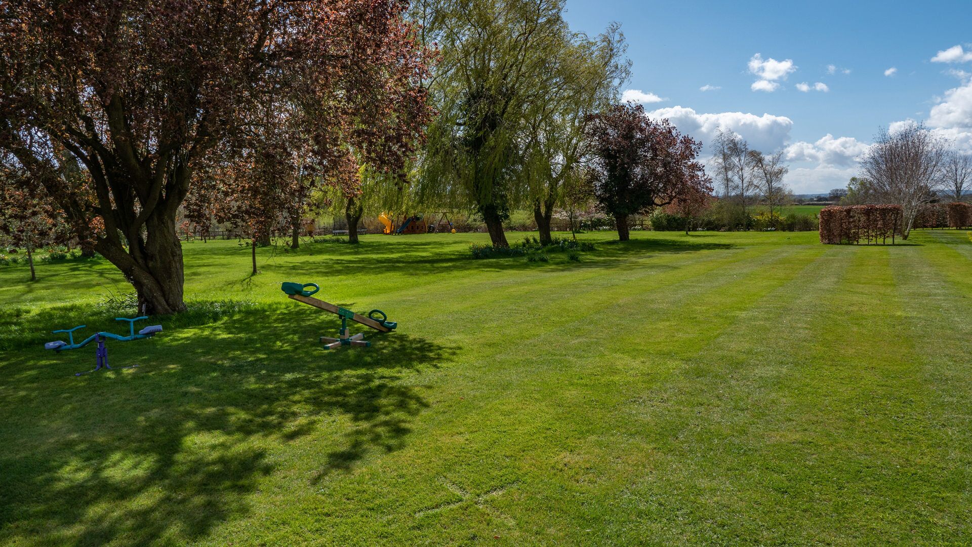 A park with a grassy field, trees, and playground equipment.
