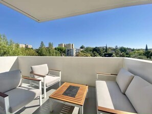 Ein Balkon mit einer weißen Couch, zwei Stühlen und einem kleinen Holztisch.