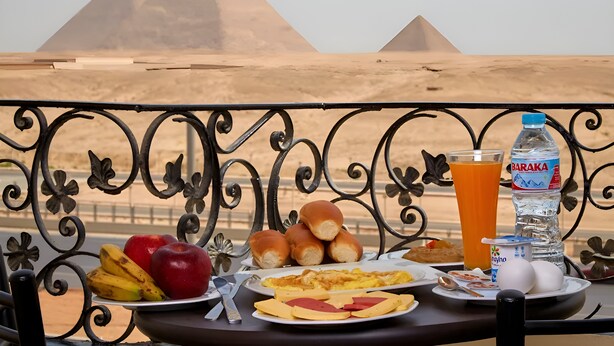 A table with breakfast items and a water bottle, set against a view of pyramids. - Pyramids planet hotel (Giza)