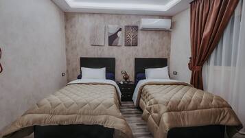 A hotel room with two beds, a ceiling light, a wall-mounted air conditioner, and a window with curtains.