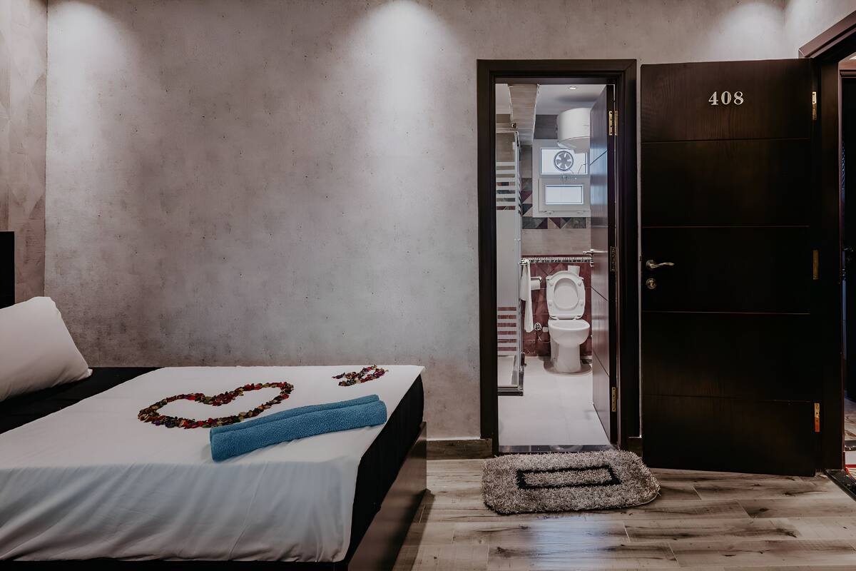 Una habitación de hotel con una cama, un baño visible a través de una puerta abierta y una puerta de madera oscura con el número 408.
