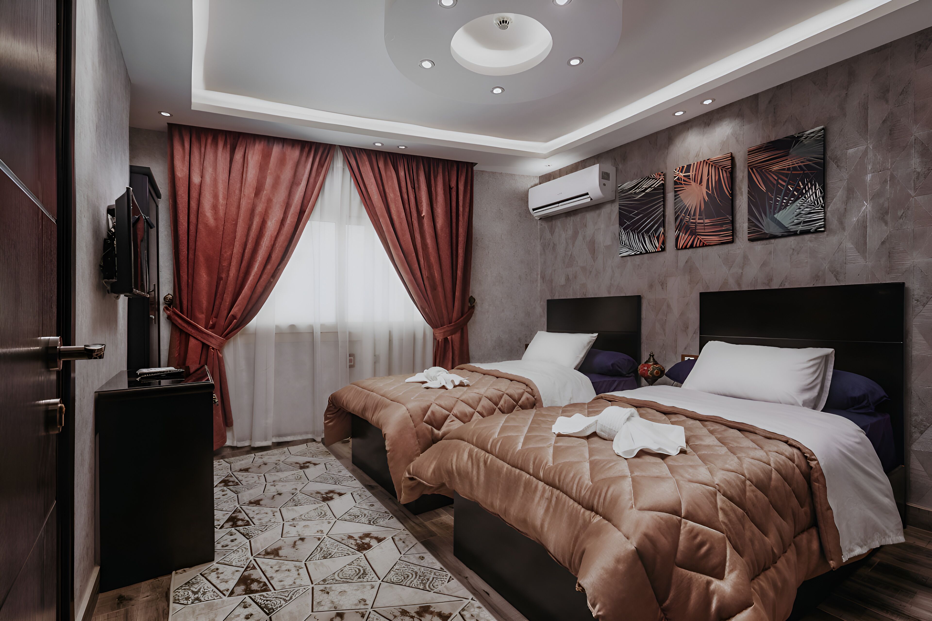 A hotel room with two beds, a TV, an air conditioner, and a decorative wall.