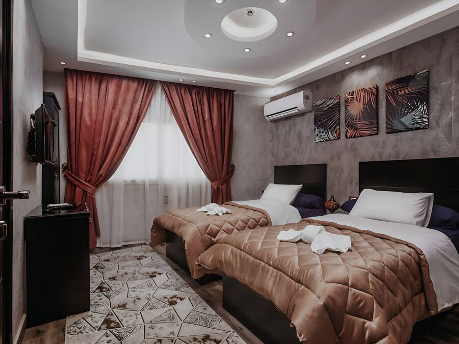 A hotel room with two beds, a TV, an air conditioner, and a decorative wall.