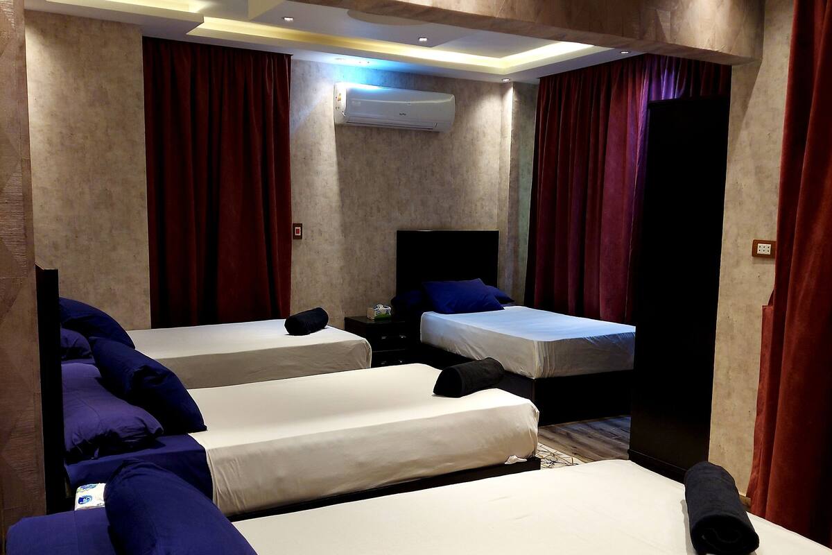 Una habitación de hotel con tres camas, cortinas rojas y un equipo de aire acondicionado.