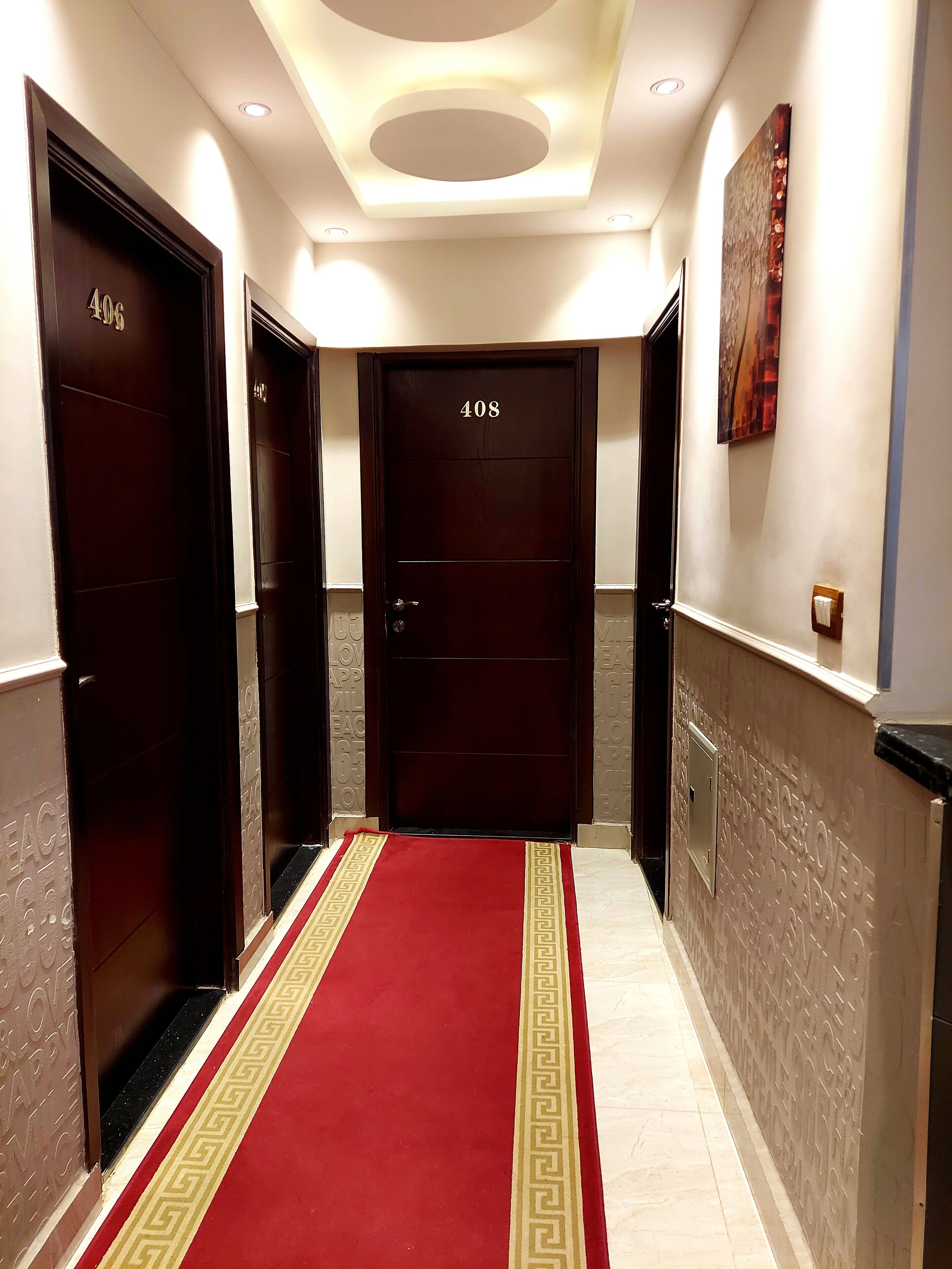 A hallway with a red carpet, three doors labeled 406, 407, and 408, and a ceiling with recessed lighting.