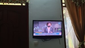 A television mounted on a wall displaying a news broadcast. - Hotel O Vj Sweethome Syariah (Mataram)