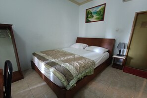 A neatly made bed with a patterned bedspread and pillows, a small bedside table with a lamp, and a painting on the wall. - Hotel O Vj Sweethome Syariah (Mataram)