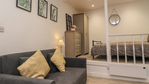 A bedroom with a bed, a nightstand, a dresser, and a mirror on the wall. - Basement Flat 43 (Keighley)
