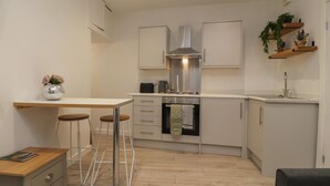 A compact kitchen with a central island, a built-in oven, and a stainless steel range hood. - Basement Flat 43 (Keighley)