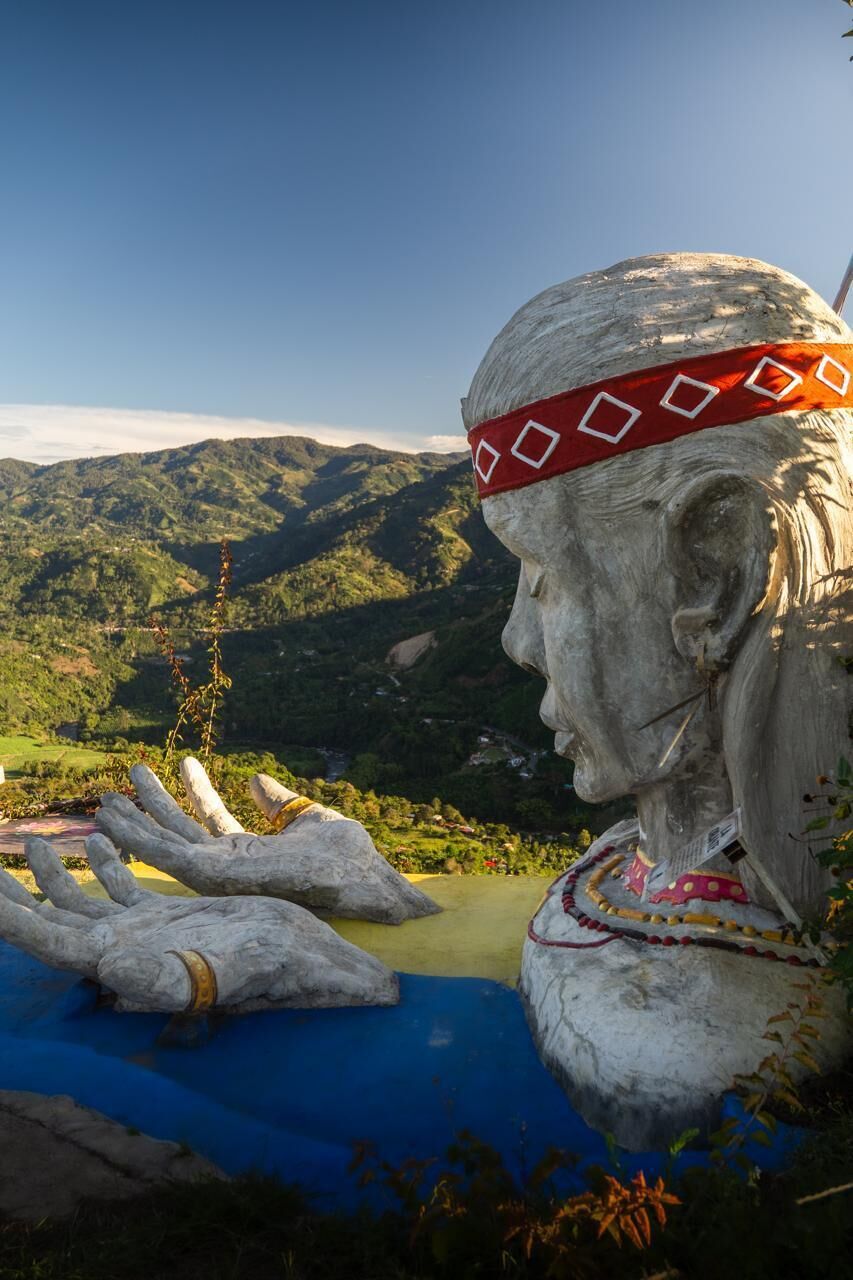 A sculpture of a figure with a red patterned headband, set against a mountainous backdrop.