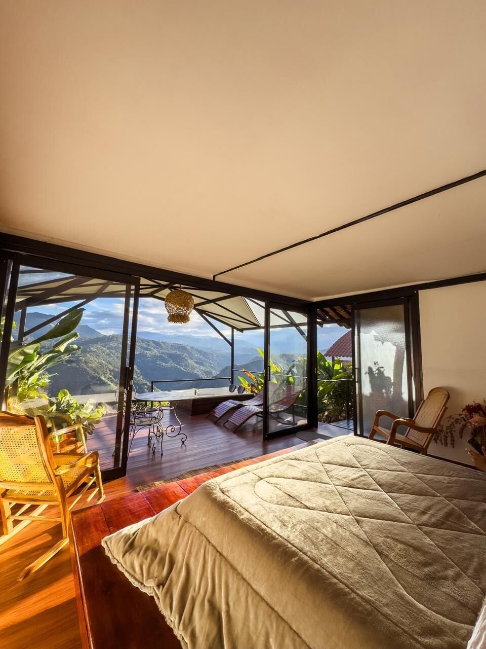 Een slaapkamer met een groot bed, uitzicht op bergen en een balkon met zitplaatsen.
