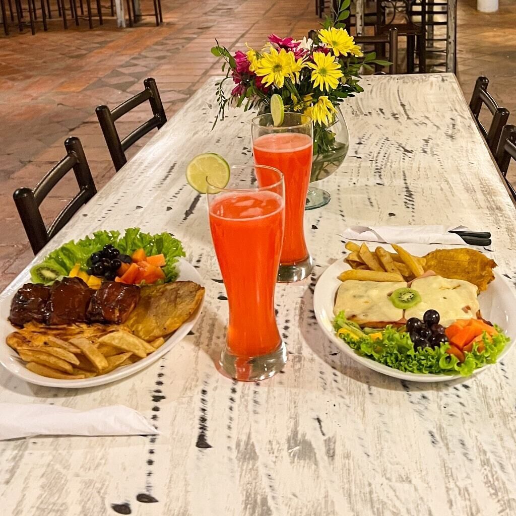 A dining table with two plates of food, a glass of red drink, and a vase of flowers.