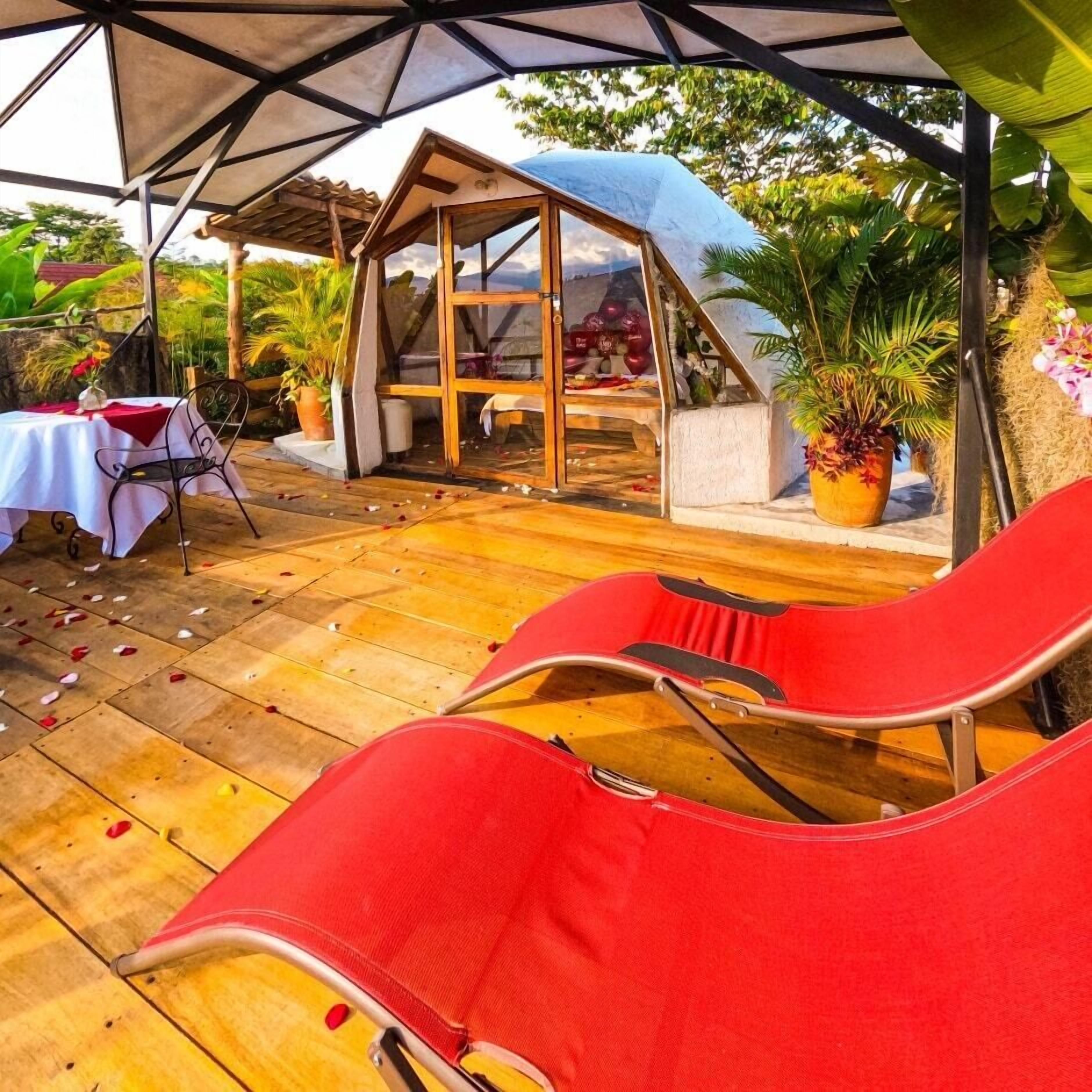 A covered patio area with wooden flooring, a small wooden structure, and red lounge chairs.