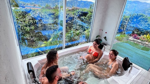 Ein Whirlpool mit drei Personen darin, große Fenster mit Blick auf Berge und Grünland.