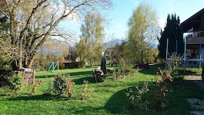 A well-maintained garden with a variety of plants and trees, a wooden bench, and a stone structure. - Chalet avec grand jardin en Chartreuse (Alpes) (Miribel-les-Échelles)