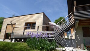 A modern building with a wooden facade, a staircase, and a garden with purple flowers. - Chalet avec grand jardin en Chartreuse (Alpes) (Miribel-les-Échelles)