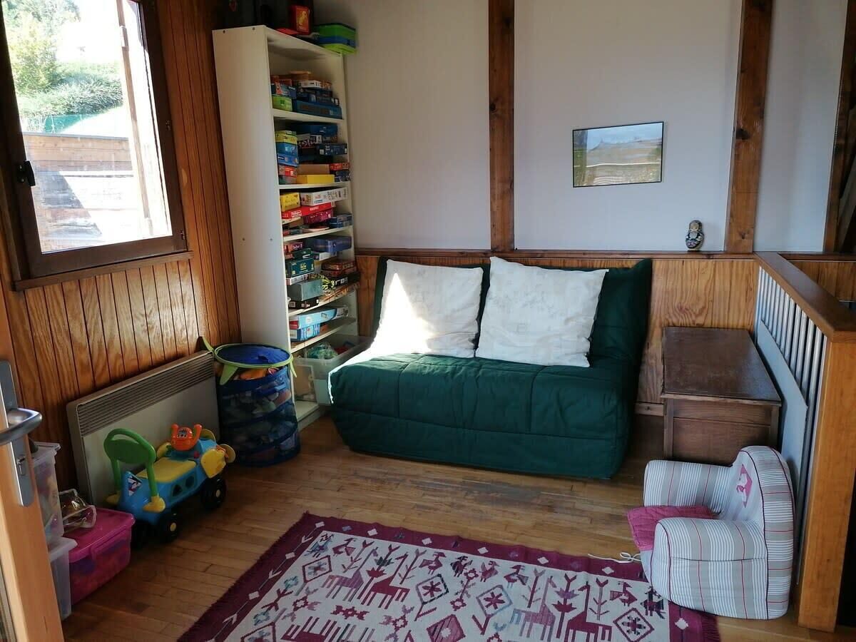A cozy room with a green sofa, a small striped chair, a toy car, and a bookshelf filled with books and toys.