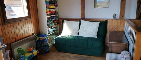 A cozy room with a green sofa, a small striped chair, a toy car, and a bookshelf filled with books and toys.