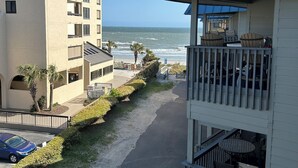 A beachfront hotel with a balcony overlooking the ocean, a parking area, and a building with multiple balconies.