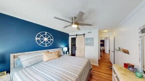 A bedroom with a bed, a ceiling fan, a compass wall decoration, and a wooden floor.