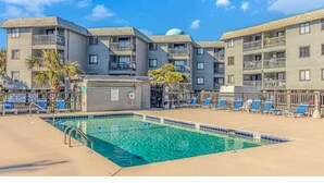 A pool area with a clear blue pool, lounge chairs, and a building with multiple balconies.