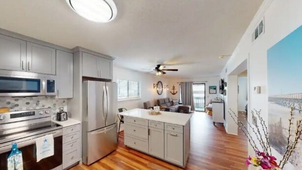 A modern kitchen with stainless steel appliances, a central island, and wooden flooring.