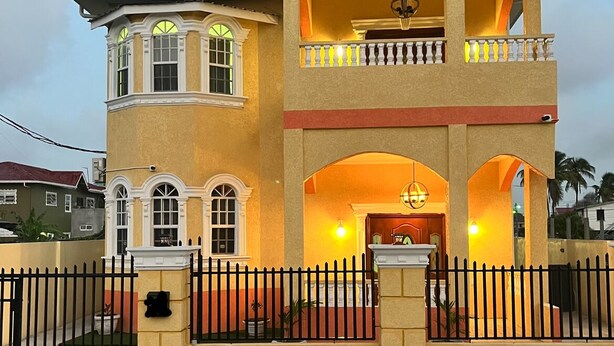 Un immeuble de deux étages doté d’un balcon à l’étage supérieur, d’une entrée sécurisée par un portail et d’un intérieur bien éclairé.