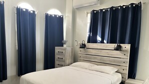 Une chambre à coucher avec un cadre de lit en bois, une table de chevet et un petit meuble à poser près du lit, ainsi que des rideaux foncés.